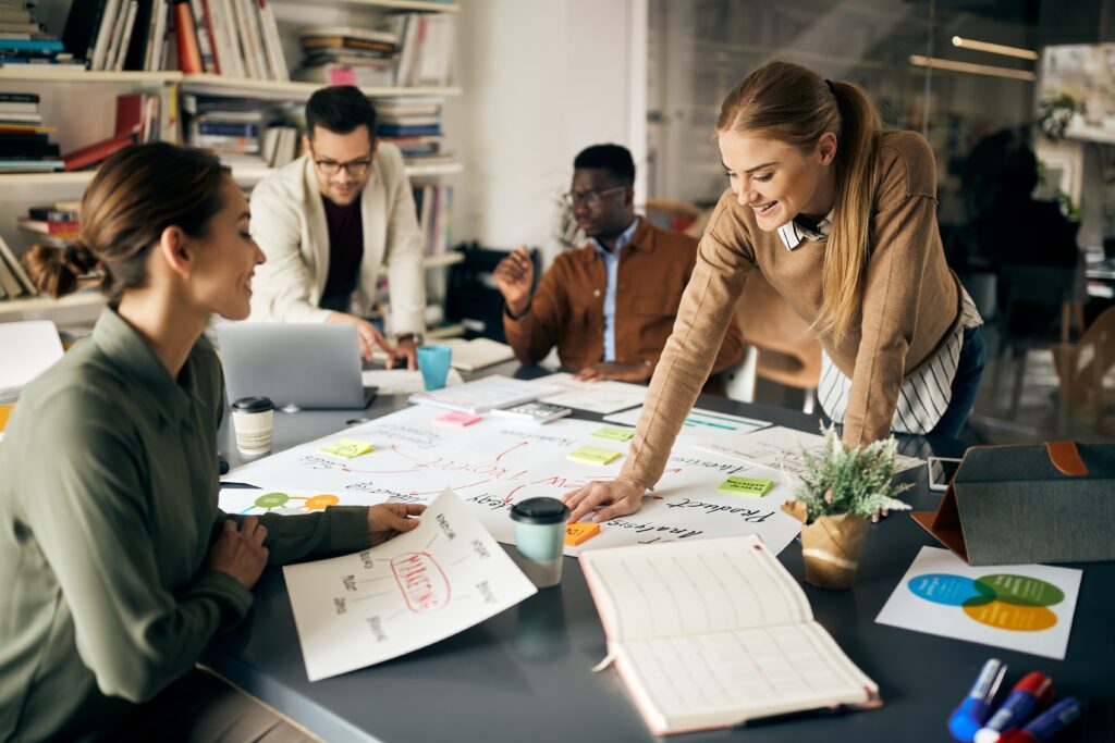 Équipe de quatre collaborateurs penchés sur une grande feuille de planification stratégique posée sur une table de réunion