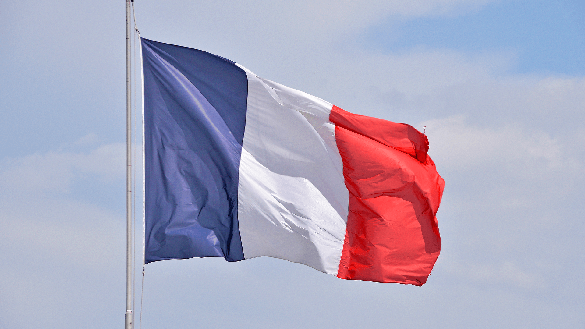 Drapeau tricolore français flottant au vent sur fond de ciel nuageux, symbole de la souveraineté nationale.