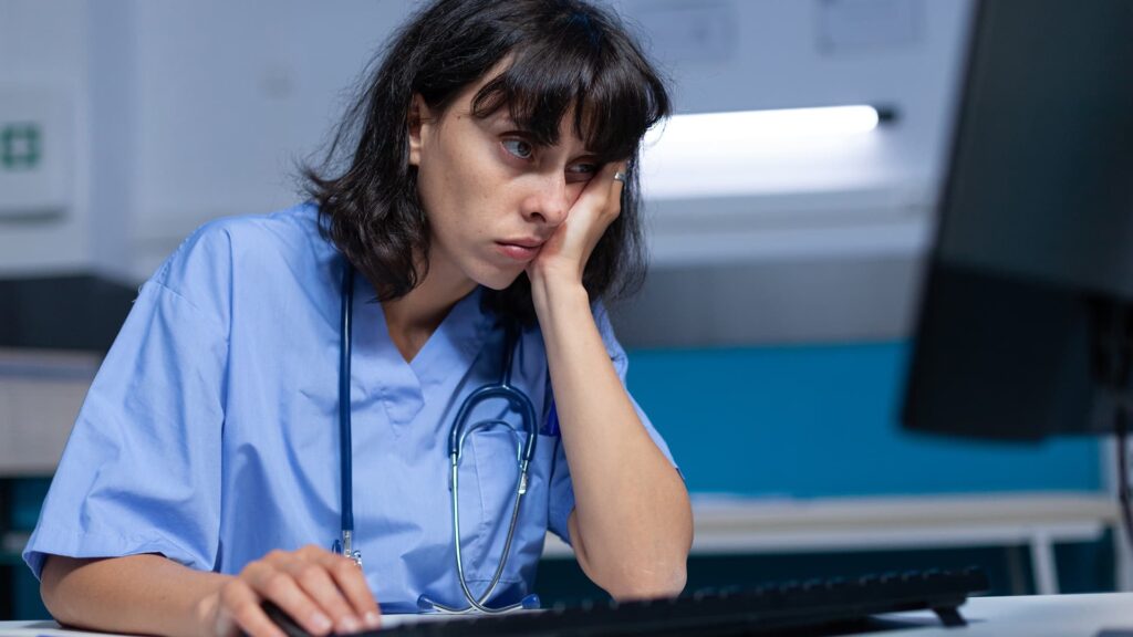 Infirmière fatiguée consultant sa boîte mail saturée sur ordinateur.