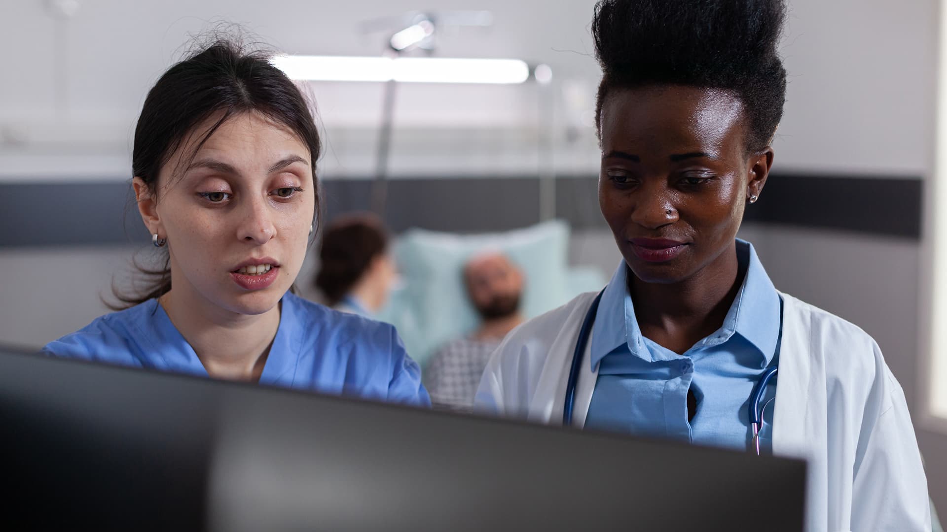 Deux professionnelles de santé échangeant devant un écran à l'hôpital