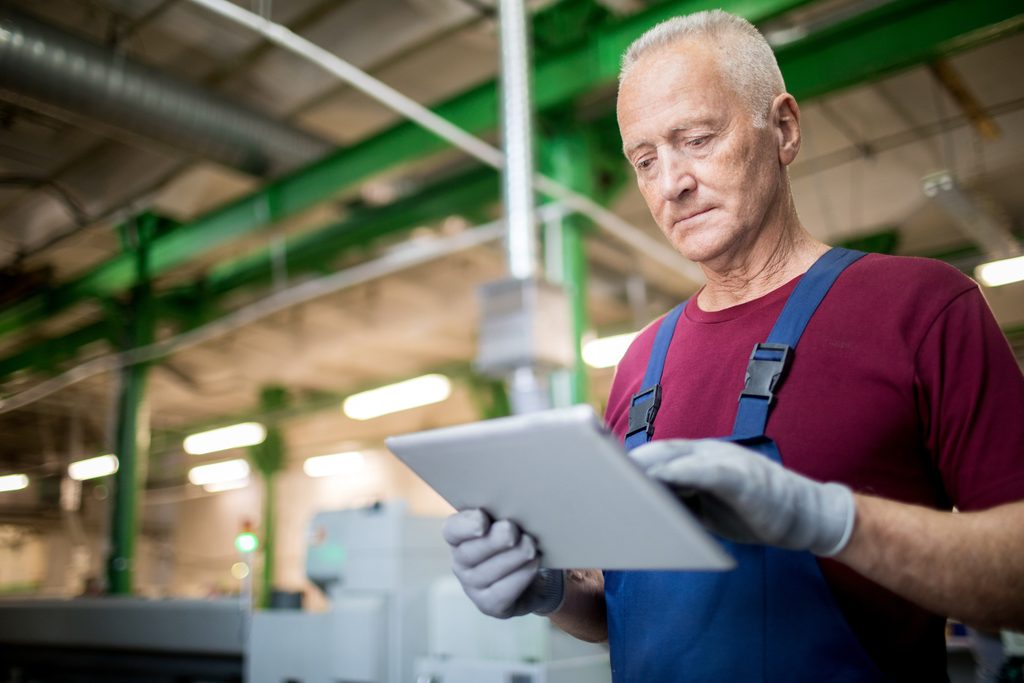 Opérateur en usine consultant une tablette, sur son lieu de travail
Titre : Communiquer avec les équipes de terrain
