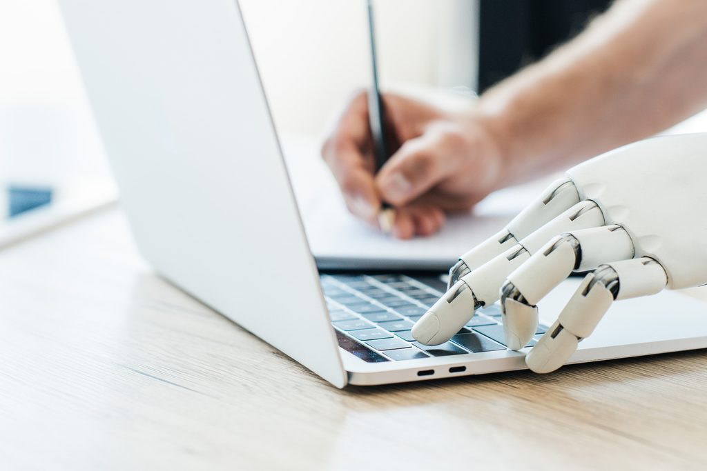 Main robotique tapant sur un clavier pendant qu’une main humaine prend des notes.